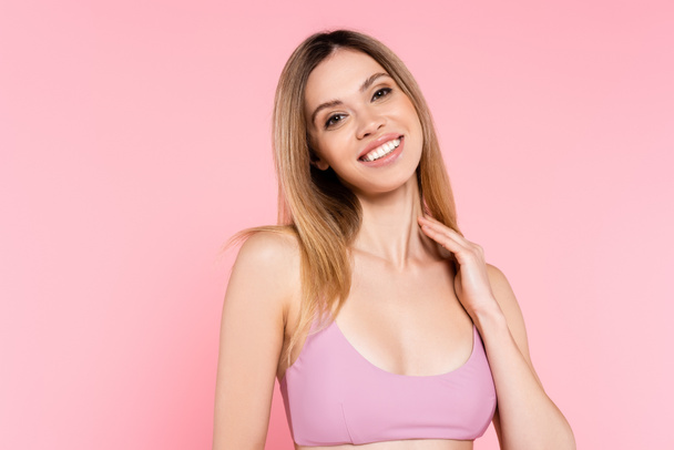Smiling woman in top of swimsuit looking at camera isolated on pink  - Фото, изображение