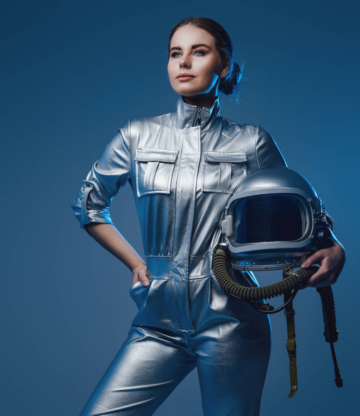 Young spacewoman in silver suit holding helmet - 写真・画像