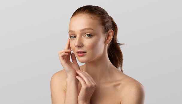 Junge weibliche Berührung Gesicht Pflege für Haut über grauem Hintergrund - Foto, Bild