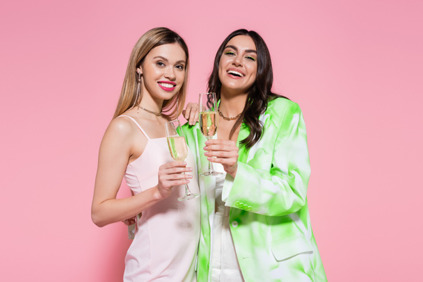 Pretty friends with champagne smiling at camera on pink background  - Фото, зображення