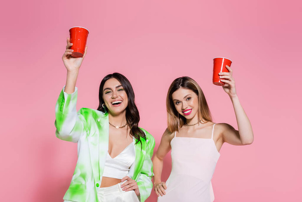 Cheerful friends holding plastic cups on pink background  - Фото, зображення