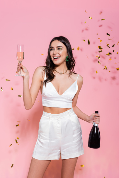Smiling woman holding champagne near golden confetti on pink background  - Foto, immagini