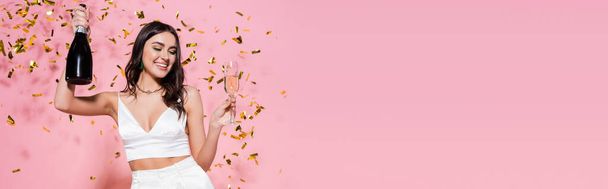 Stylish woman with champagne near festive confetti on pink background, banner  - Fotó, kép