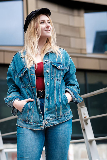 Portrait of young woman posing with a banister behind her. She is wearing denim jacket and trousers. - Foto, Imagen