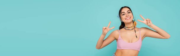 Smiling woman in top showing victory gesture isolated on blue, banner  - Фото, зображення