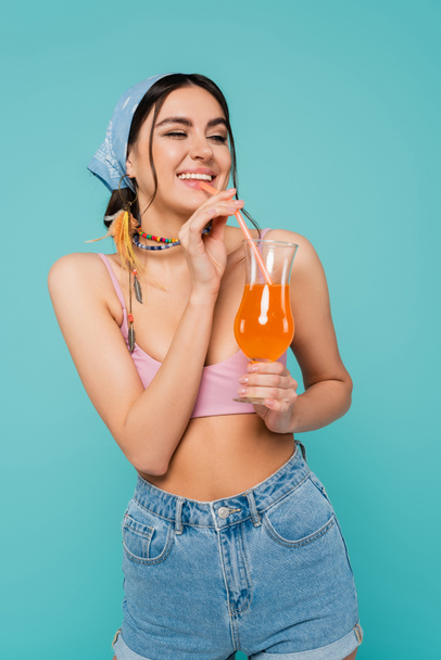 Pretty woman in top and bandana drinking cocktail isolated on blue  - Foto, immagini