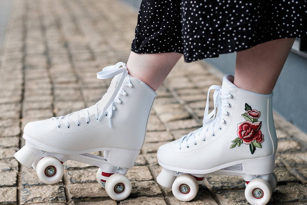 Vista cercana a las piernas femeninas con patines de ruedas. Son blancos y están en el pavimento de piedra. - Foto, Imagen