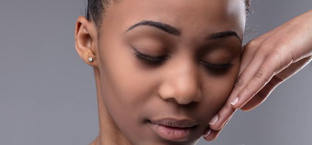 Portrait tendre et sensuel d'une jeune femme noire aux yeux abattus, touchée doucement sur la joue par la main d'une femme dans une démonstration d'empathie, d'amour et de soutien - Photo, image
