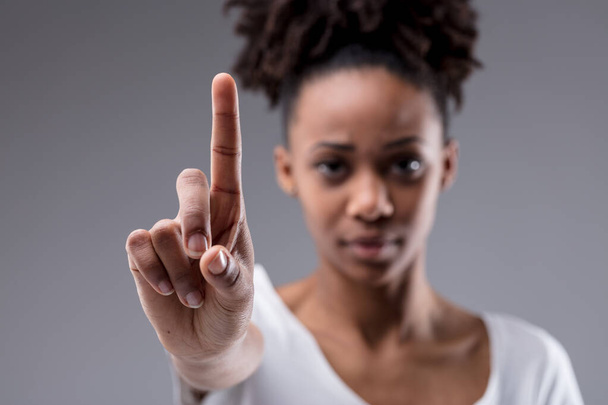 Стерн сосредоточена молодая женщина, держа указательный палец, как бы подчеркивая точку, вызывая остановку, или идентифицируя себя на сером фоне студии - Фото, изображение