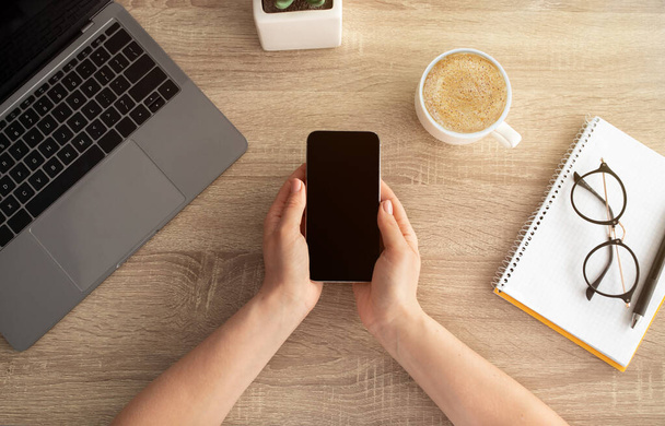 Žena drží smartphone s prázdnou obrazovkou pro váš design nebo reklama, dřevěný stůl pozadí, horní pohled - Fotografie, Obrázek