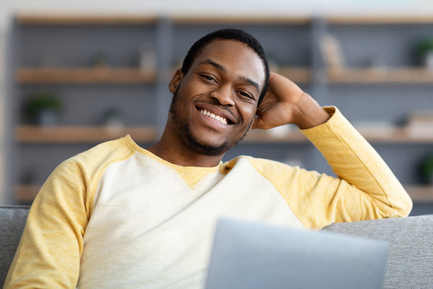 Крупный план черного парня с ноутбуком, улыбающегося в камеру - Фото, изображение