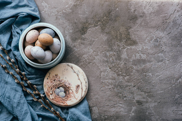 Vintage background with easter eggs in wooden plate on a concrete background. Napkin and spring branches. Top view with copy space. - Photo, image