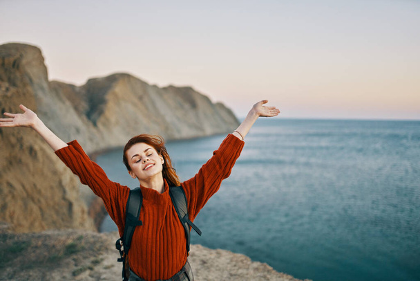 onnellinen matkustaja vuorilla lähellä merta eleet käsillään ja reppu selässään - Valokuva, kuva