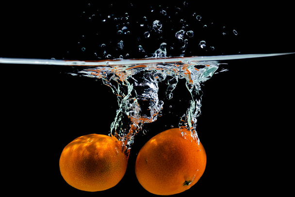 two tangerines fall into the water on a black background, copy space - Photo, Image