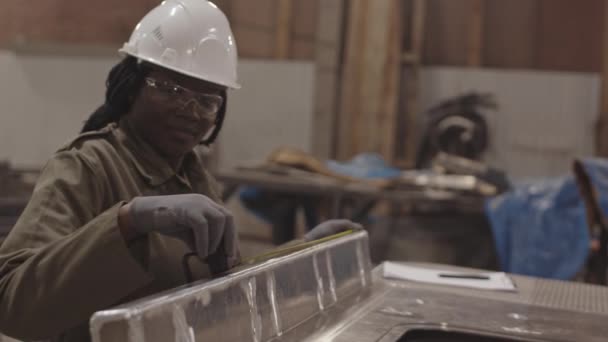 Střední detailní záběr africké pracovnice s bílým tvrdým kloboukem a bezpečnostními brýlemi, s použitím páskové míry na kovovém dílku, poté sepsání rozměrů - Záběry, video
