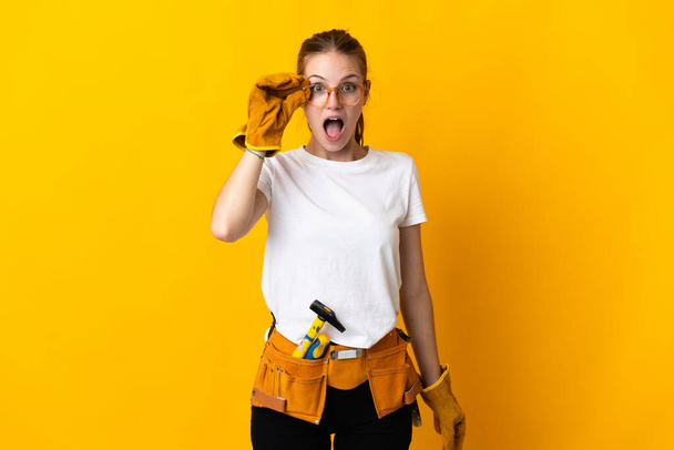 Mujer electricista joven aislada sobre fondo amarillo con gafas y sorprendida - Foto, imagen