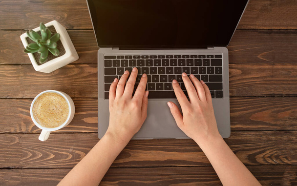 Nők kezek laptop billentyűzeten, hölgy dolgozik a számítógépen egy csésze kávé és kis növény pot fából készült asztalon - Fotó, kép