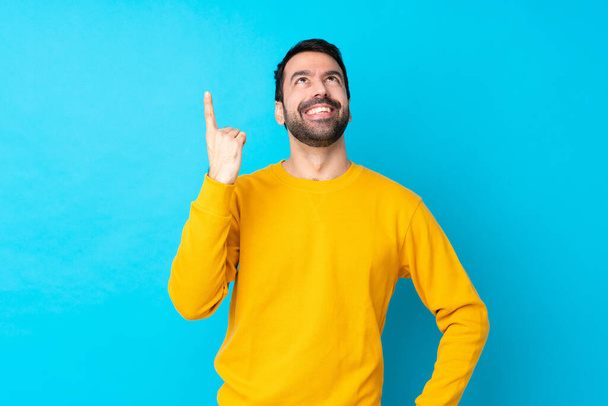 Young caucasian man over isolated blue background pointing up and surprised - Fotoğraf, Görsel