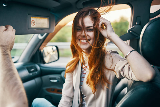 heureuse femme rousse en manteau beige sur le siège avant d'un modèle de sourire de voiture gesticulant avec ses mains compagnon de voyage - Photo, image