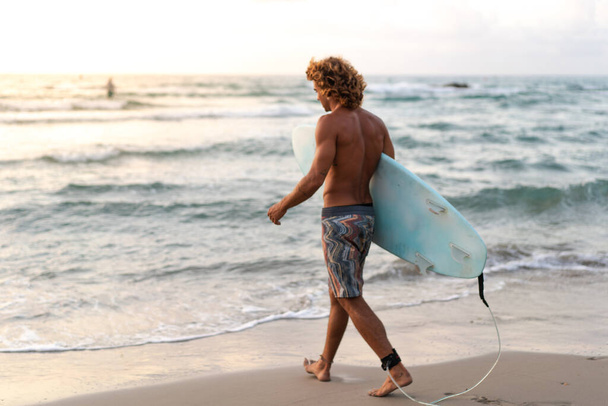 Joven caucásico hombre levantarse temprano a hacer surf al amanecer - Foto, Imagen