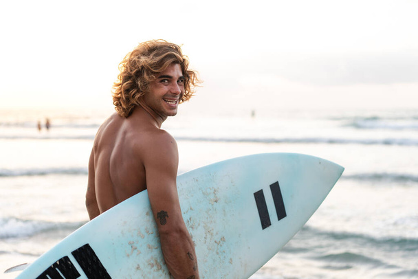 Fiatal fehér férfi korán kel szörfözni napkeltekor. - Fotó, kép