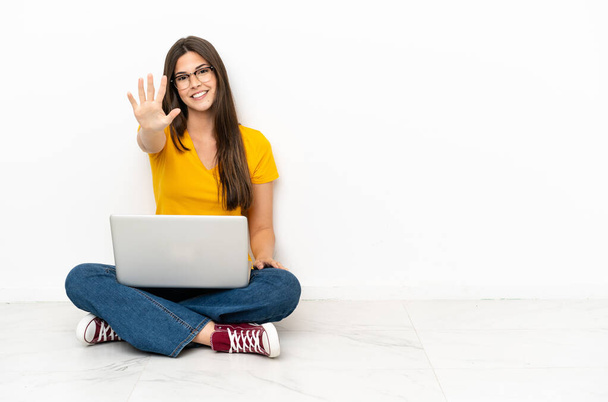 Νεαρή γυναίκα με ένα φορητό υπολογιστή που κάθεται στο πάτωμα μετρώντας πέντε με τα δάχτυλα - Φωτογραφία, εικόνα