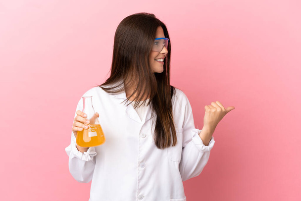 Νεαρή επιστημονική κοπέλα πάνω από απομονωμένο ροζ φόντο που δείχνει προς τα πλάγια για να παρουσιάσει ένα προϊόν - Φωτογραφία, εικόνα