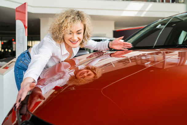 Beautiful woman hugging her new car in dealership. - Zdjęcie, obraz