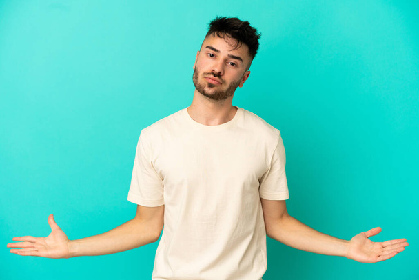 Young caucasian man isolated on blue background having doubts - Photo, Image