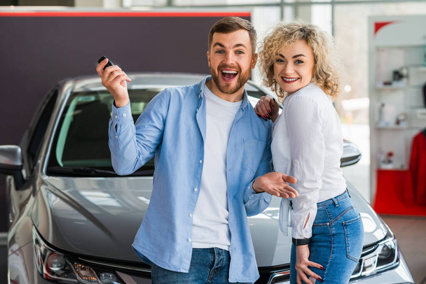 Szczęśliwa para w salonie samochodowym na tle ich nowego samochodu - Zdjęcie, obraz