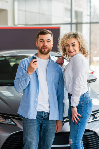 Glückliches Paar im Autohaus vor dem Hintergrund seines neuen Autos - Foto, Bild