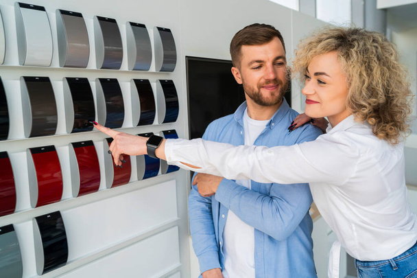Family couple in car dealership choosing the color of their new car. Man and woman looking color samples of car body - 写真・画像