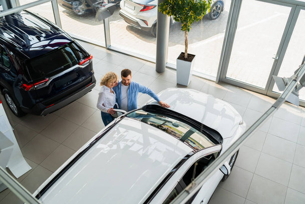 Hombre y mujer en un concesionario de coches vista superior. Pareja eligiendo su nuevo coche - Foto, imagen