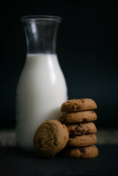 Vista de cerca de galletas de chispas de chocolate y una botella de leche con migajas en la mesa de madera simple desayuno por la mañana snack - Foto, Imagen
