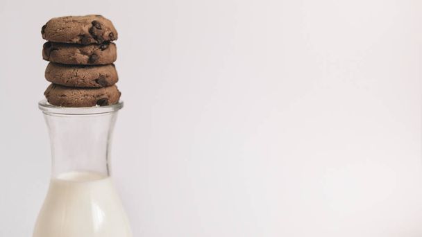 Vista de cerca de la galleta de chocolate chip de pie en una botella de leche sobre fondo blanco simple merienda de la mañana copiar el texto del espacio - Foto, imagen