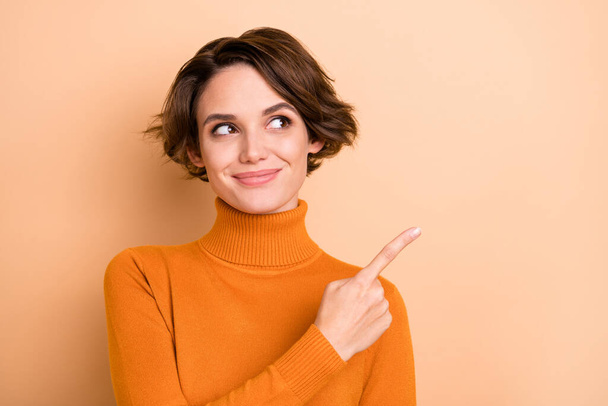 Photo of adorable sweet young girl orange turtleneck looking pointing finger empty space isolated beige color background - Foto, afbeelding