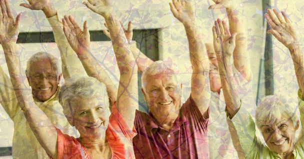 Composition of senior group raising hands, smiling and autumn foliage. healthy active retirement lifestyle concept digitally generated image. - Foto, imagen
