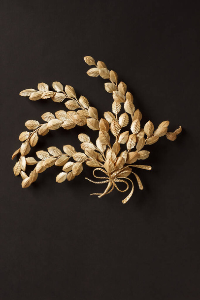 The branch with leaves is made of straw. Straw wall decoration. The products are made of straw. Decoration of straw on a dark background. - Photo, image