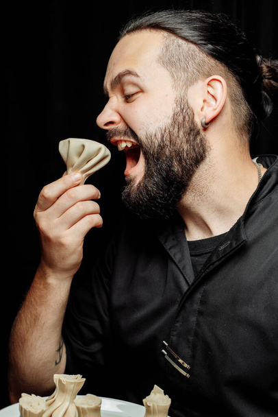 Ο γενειοφόρος τρώει συναισθηματικά χινκάλι. Το εθνικό γεωργιανό πιάτο khinkali. Έννοια της διαφημιστικής φωτογραφίας του khinkali - Φωτογραφία, εικόνα