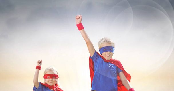 Composition of smiling caucasian boy and girl in superhero costumes with arms in air celebrating. sport, fitness and active lifestyle concept digitally generated image. - Фото, изображение
