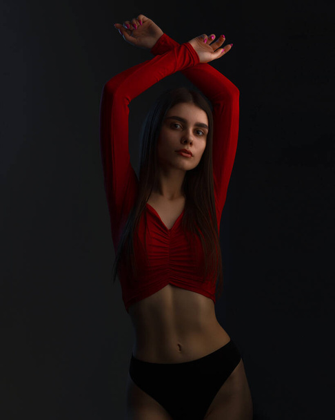 Young woman posing in a red top shirt and black panties, on black background in studio. Seductive woman perfect body. Sexy fashion model wear black underwear. - Фото, зображення