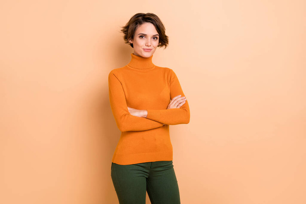 Photo of adorable serious young girl orange turtleneck arms crossed isolated beige color background - Фото, зображення