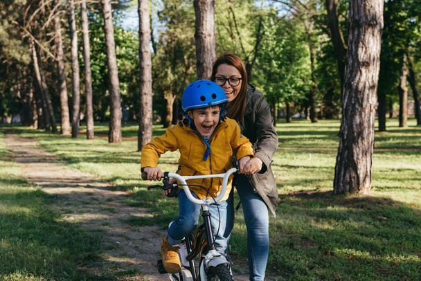 mother helps her boy to ride a bike in public park - 写真・画像