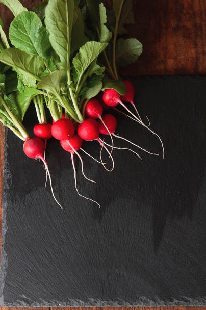 fresh radish with stems and leaves lies on a black granite pedestal board - Photo, Image