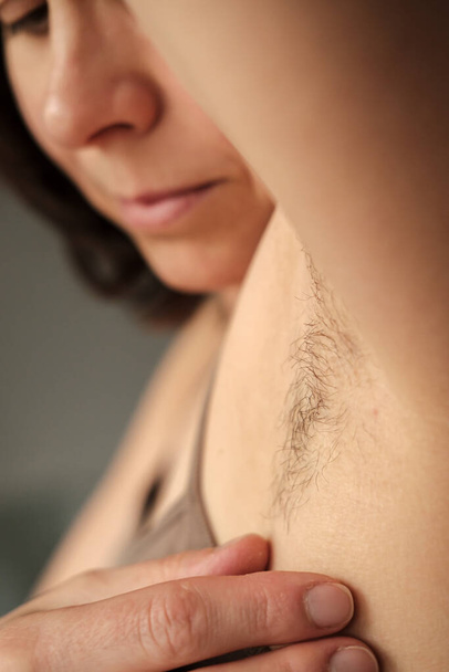 Szőrös, borotválatlan női hónalj egy női arc homályos hátterén. A test pozitív koncepciója és természetességének elfogadása.  - Fotó, kép