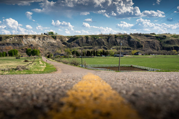 The centre line of paved country road along the South Saskatchewan river valley near Medicine Hat Alberta Canada under a cloudy blue sky. - Foto, Imagem
