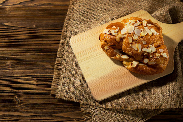 Croissants mit Mandelflocken auf dem Holzteller und einem Tuch. traditionelles französisches Frühstück mit frischer Bäckerei - Foto, Bild