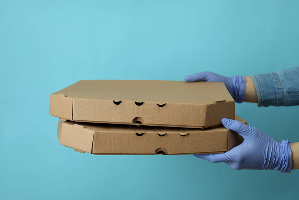 Las manos en los guantes sostienen cajas de pizza sobre fondo azul - Foto, imagen
