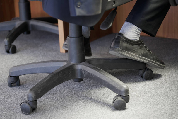 Ноги дежурного клерка или диспетчера сидят на пневматическом стуле с колесами. Концепция офисной мебели и ее использование. Выборочный фокус. Крупный план - Фото, изображение