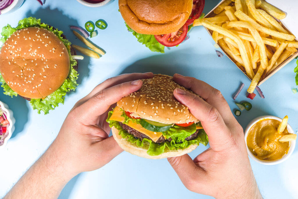 Еда, концепция бургерной вечеринки. Разнообразные вкусные гамбургеры с картошкой фри и соусами на ярко-голубом фоне - Фото, изображение